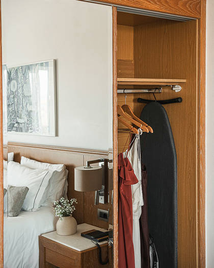 Wooden wardrobe with mirrored door, hangers and ironing board, reflecting the bed