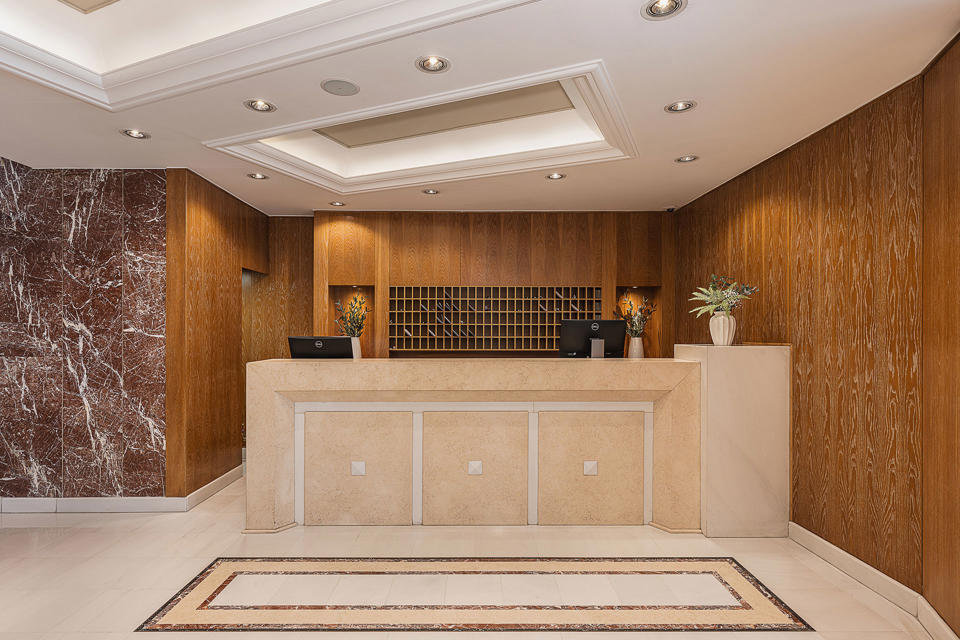 Reception desk in stone and warm wood, with marble flooring, an inlaid mosaic strip and soft ceiling lighting