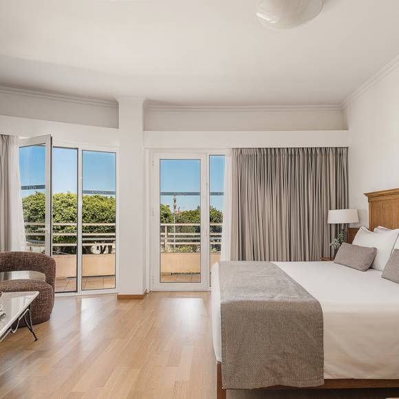 Junior Suite with king size bed and floor-to-ceiling windows opening onto a balcony with sea view