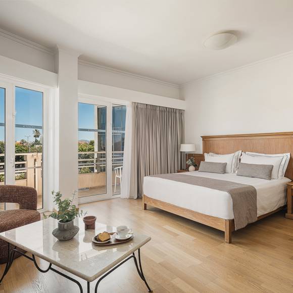 Junior Suite with king size bed and seating corner beside floor-to-ceiling windows facing the sea
