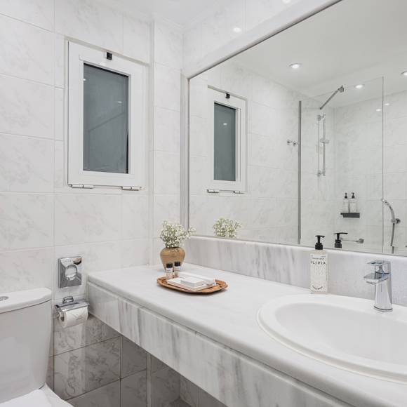 Marble bathroom with wide mirror, washbasin and toiletries beside a window with natural light