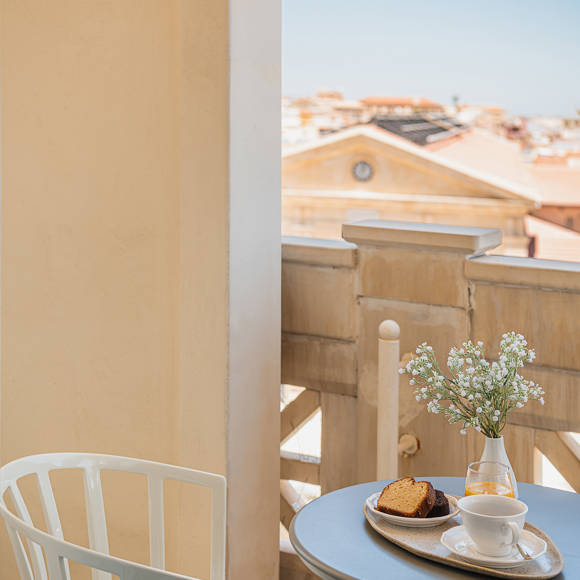 Private balcony table set with breakfast and fresh flowers, overlooking the Old Town rooftops