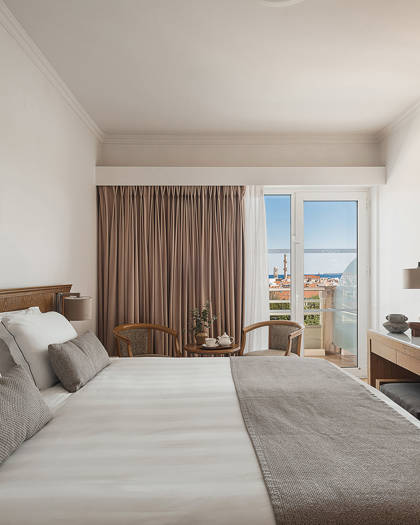 Room with double bed, seating area by the balcony and desk with TV, overlooking the Old Town