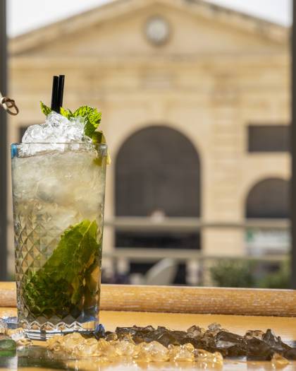 Mojito cocktail with fresh mint and crushed ice on the bar, with the Municipal Market building behind